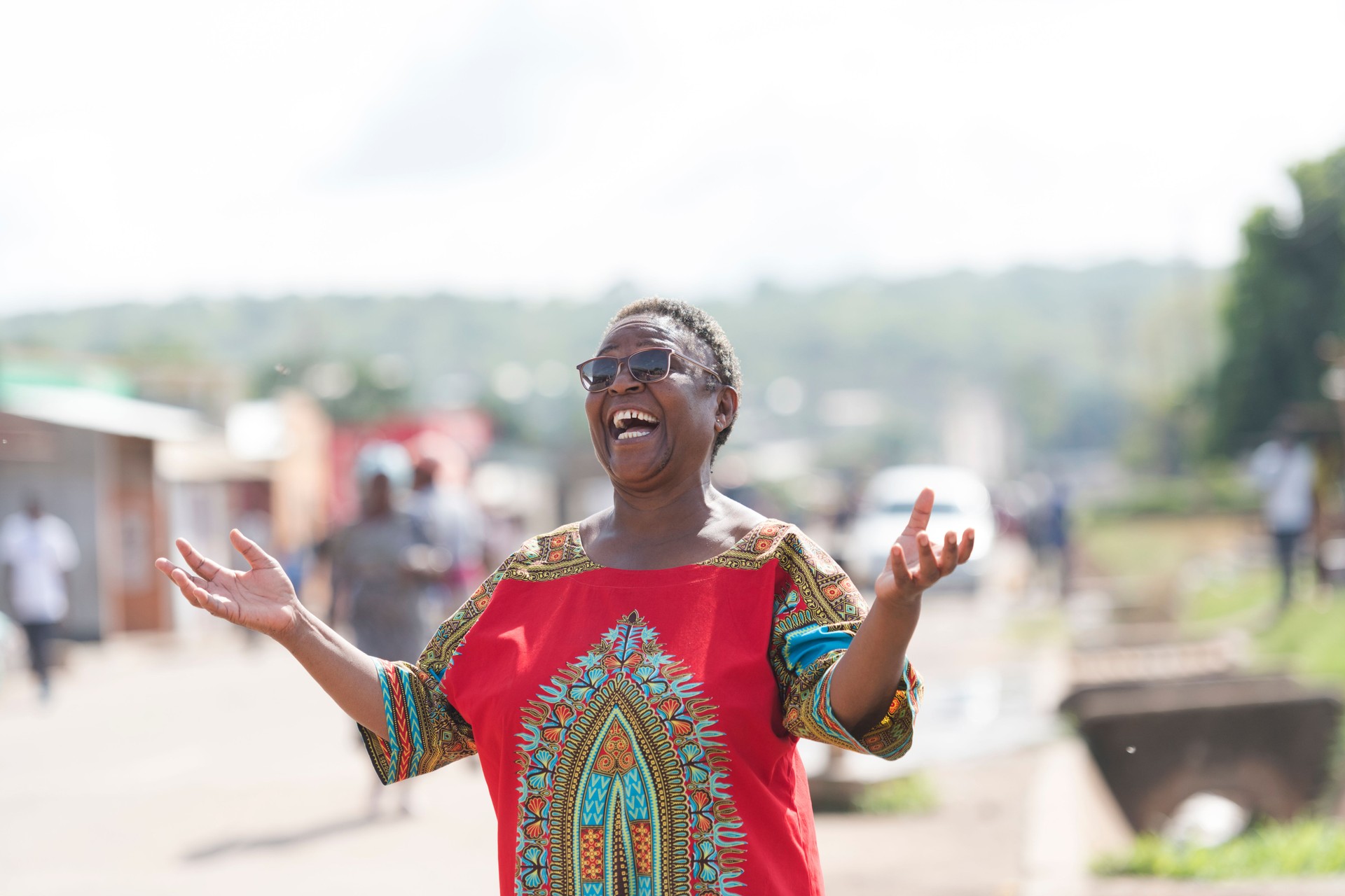 Senior African woman laughing hands raised on rural street
