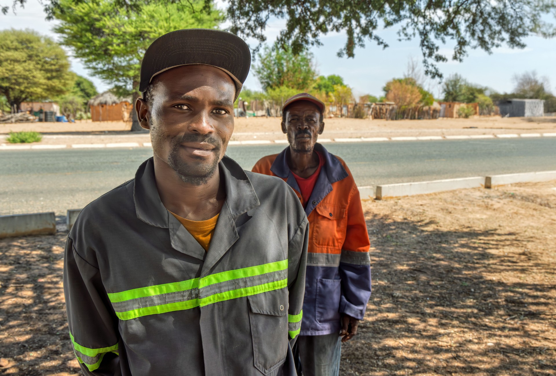 african village, two man wearing workwear and hats, outdoors, villagers in the township in the street